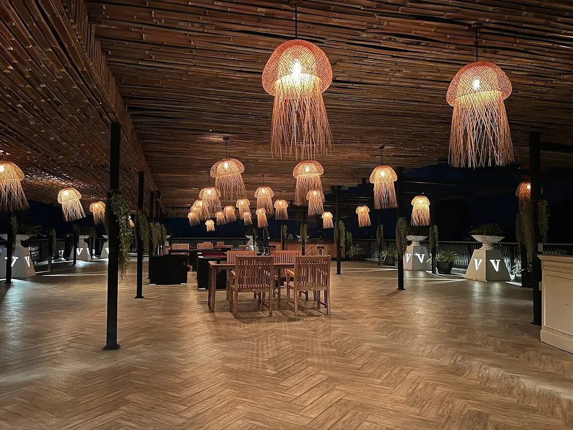 The beachfront dining pavilion at night, woven pendant lamps overhead
